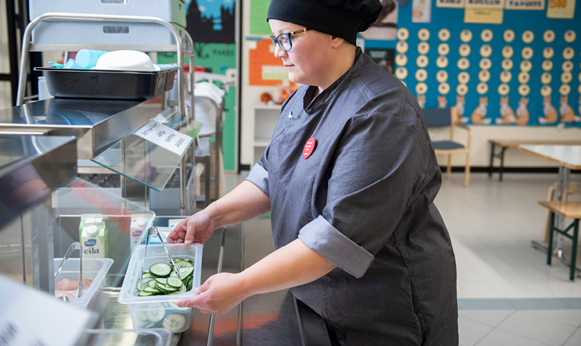 An employee from Servica's food services sets down sliced cucumbers on the food serving line.