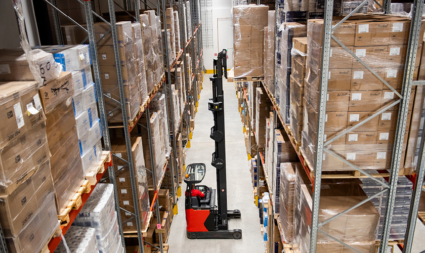 A forklift truck at the central warehouse of Servica lifts a pallet with cardboard boxes onto the top shelf.