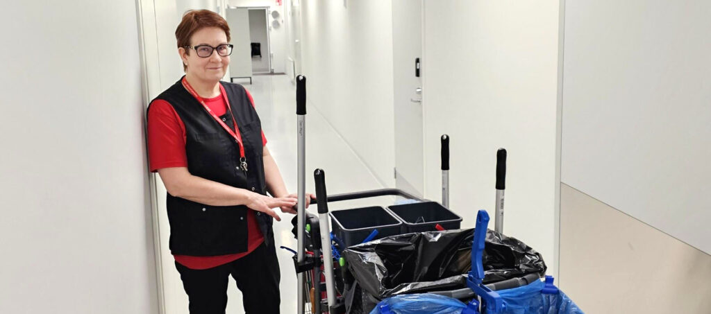 Tuija Miettinen, Facility Cleaner at Servica, in a corridor next to a cleaning trolley.