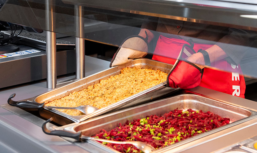 An employee of Servica's food services presents hot food on the serving line.